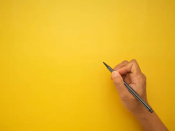 Hand woman holding of black pen on yellow background. Space for text. Top view.