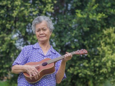Bahçede dikilirken ukulele çalan kısa gri saçlı son sınıf bir kadının portresi. Emekli olduktan sonra hayatın tadını çıkar. Yaşlılar ve rahatlama kavramı.