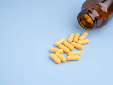 Açık mavi arka planda cam bir şişenin dışında sarı kapsül hapları yığını. Mesaj için yer var. Tıp konsepti.