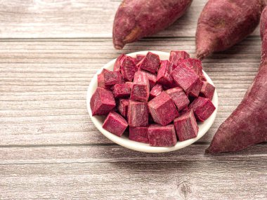 Ahşap bir masada, üzerinde metin için fotokopi alanı olan bir kasede doğranmış yer elmaları olan mor yer elması yığını. Mor tatlı patates. Üst Manzara. Vejetaryen meyve ve sağlıklı meyve kavramı.