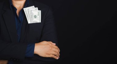 İş adamı takım elbisesinin cebinde Amerikan doları olan bir takım elbise giyiyor ve stüdyoda siyah bir arkaplan ve mesaj için yeri olan kolları çapraz duruyor. İş ve finans kavramı.
