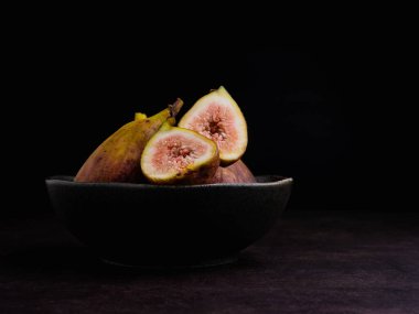 Olgun incirler ve kesilmiş meyveler siyah arka planlı, antika bir zeminde, siyah bir klozetin üzerinde. Yüksek vitamin meyvesi. Yakın plan fotoğraf. Sağlıklı meyve ve sağlık konsepti.