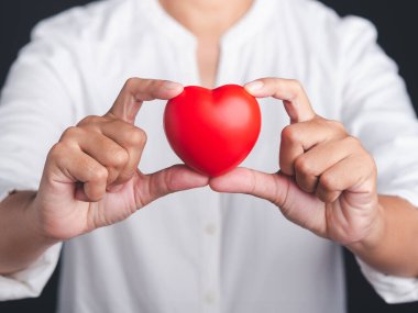 Stüdyoda siyah bir arka planda dururken kırmızı kalp şeklini tutan bir el. Yakın plan fotoğraf. Mesaj için yer var. Bağış, aşk ve teşvik konsepti.