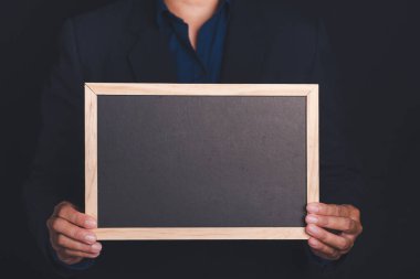 Stüdyoda siyah bir arka planda dururken elinde küçük bir karatahta tutan bir iş adamının eli. Mesaj için yer var. Yakın plan fotoğraf..