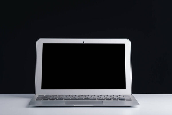 Laptop with blank screen on white table with a black background. Space for text.
