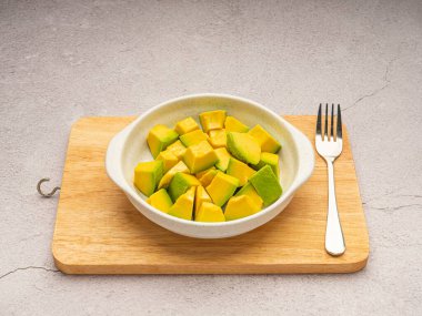 Seramik kasede kesilmiş avokadolar ve çimento arka planında tahta kesme tahtasındaki çatal bıçak takımı. Yakın plan fotoğraf. Üst Manzara. Yüksek vitamin meyvesi. Sağlıklı meyve kavramı.