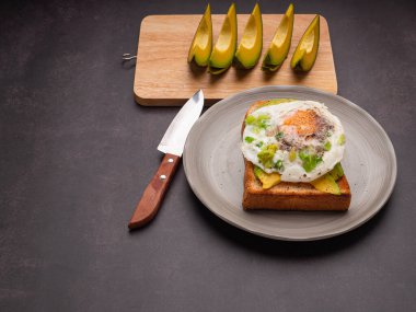 Avokado ve yumurtalı tost tabakta servis edilir. Avokado, tahta bir kesme tahtasının üzerinde bıçakla dilimlenmiş. Üst Manzara. Mesaj için yer var. Yüksek vitamin meyvesi. Sağlıklı meyve kavramı.