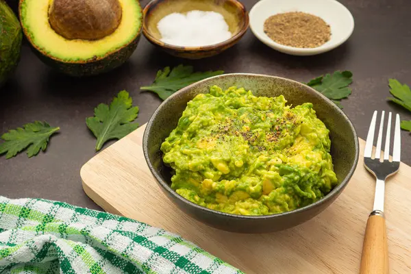Tahta kesme tahtasının üzerinde bir kaseye Guacamole sosu ve klasik arka plandaki malzeme. Meksika yemekleri ve sağlıklı avokado meyvesi kavramı
