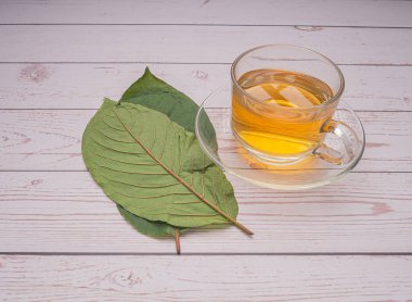 Mitragyna Speciosa veya Kratom 'un en üst görüntüsü, metin için kopyalama alanı olan ahşap bir masada bir çay fincanıyla ayrılıyor. Yakın plan fotoğraf. Tıbbi ve bitkisel konsept.