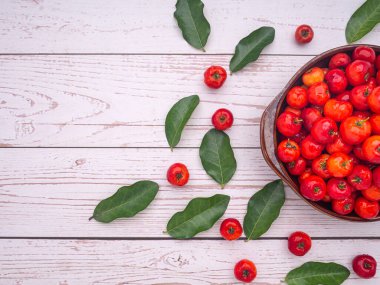 Olgun kırmızı acerola kirazları seramik bir kasede meyve ve ahşap bir masada yeşil yapraklar. Yüksek C vitamini ve antioksidan meyveler. Yakın plan fotoğraf. Mesaj için yer var. Sağlıklı meyve kavramı.