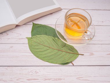 Mitragyna Speciosa veya Kratom 'un en üst görüntüsü bir çay fincanı ve metin için kopya alanı olan ahşap bir masanın üzerinde bir kitapla ayrılıyor. Yakın plan fotoğraf. Tıbbi ve bitkisel konsept.