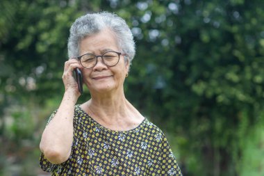 Mutlu, güzel, son sınıf öğrencisi bir kadın akıllı telefon kullanıyor ve bahçede dikilirken kameraya gülümsüyor. Mesaj için yer var. Yaşlılar ve iletişim konsepti.