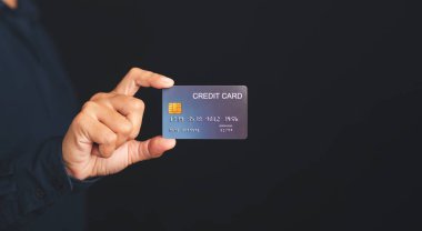 Stüdyoda siyah bir arka planı olan mavi bir kredi kartını tutan el. Yakın plan fotoğraf. Para ve iş konsepti.