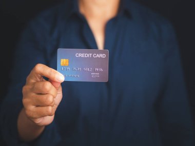 Stüdyoda siyah bir arka planı olan mavi bir kredi kartını tutan el. Yakın plan fotoğraf. Para ve iş konsepti.