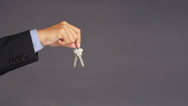 Bir iş adamının eli, mesaj veya bilgi içeriği için boş fotokopi alanı olan gri arkaplan üzerinde iki anahtar tutar..