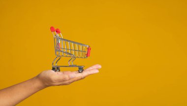 İş ve e-ticaret kavramı. Stüdyoda sarı bir arka planda dururken avuç içi kadına ait boş bir alışveriş arabasının yakın çekimi. Yan görüş. Metin için boşluk.