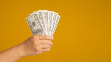 Sarı arka planda bir avuç dolusu Amerikan banknotunu tutuyor. Yakın plan fotoğraf. İş, finans ve yatırım kavramı.
