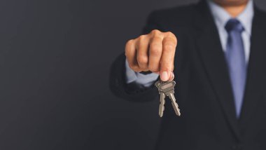 Ev kredisi ve gayrimenkul yatırım konsepti. Bir iş adamının eli, mesaj veya bilgi içeriği için boş fotokopi alanı olan gri arkaplan üzerinde iki anahtar tutar..