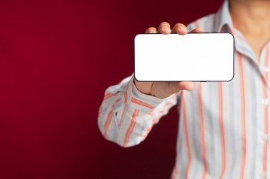 Teknoloji, iletişim ve reklam kavramı. Kırmızı arkaplan ile ayakta dururken mesaj veya bilgi için boş bir kopya alanı ekranı olan bir akıllı telefonu yakın plan tut.
