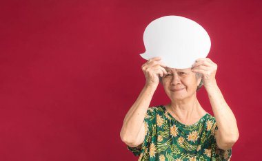 Konuşma balonu konsepti. Kısa gri saçlı, elinde balon olan ve stüdyoda kırmızı bir arka planda dururken kameraya gülümseyen son sınıf öğrencisi..