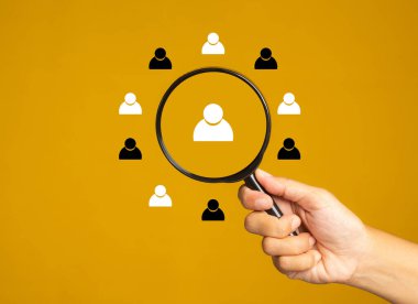 Arama konsepti. Sarı arkaplan üzerinde insan simgeleri olan bir büyüteç tutarken metin için kopyalama alanı oluşturuluyor. Yakın plan fotoğraf..