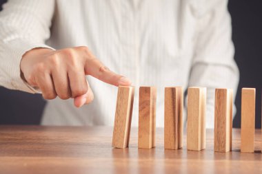 Yakın plan, tahta bir bloğu domino taşına bastır. İş konseptinde risk ve strateji.