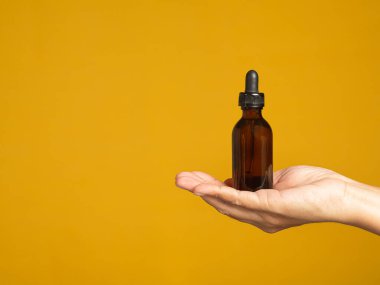 Mokup tasarım sunum konsepti. Sarı arka planda reklam için etiketi olmayan kahverengi bir şişe bardağı tutuyor. Metin için boşluk.