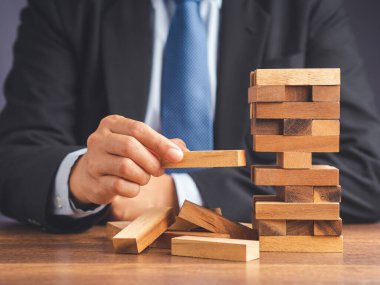 İş büyümesi ve başarı konsepti için yönetim ve strateji planları riski. Çalışma masasında otururken takım elbiseli bir işadamının tahta blok oyunu oynaması. Metin için boşluk.