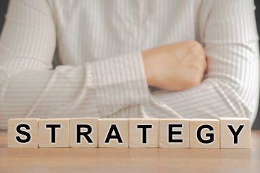 Tahta masadaki tahta küplere işadamının kollarını kavuşturarak yazılmış stratejik bir kelime. Mesaj için yer var. İş stratejisi kavramı.