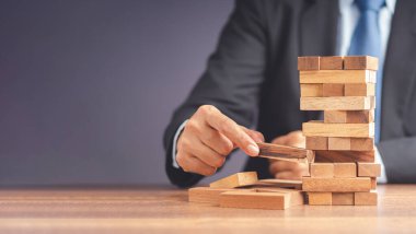 İş büyümesi ve başarı konsepti için yönetim ve strateji planları riski. Çalışma masasında otururken takım elbiseli bir işadamının tahta blok oyunu oynaması. Metin için boşluk