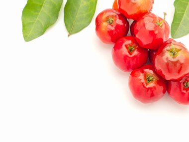 Beyaz bir zemin üzerinde olgun kırmızı acerola kirazı ve yeşil yapraklar yığını. Yüksek C vitamini ve antioksidan meyveler. Üst Manzara. Mesaj için yer var. Yakın plan fotoğraf. Sağlıklı meyve kavramı