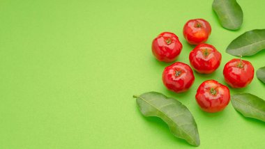 Açık yeşil zemin üzerinde olgun kırmızı acerola kirazları ve yeşil yaprakların üst görüntüsü. Yüksek C vitamini ve antioksidan meyveler. Mesaj için yer var. Yakın plan fotoğraf. Sağlıklı meyve kavramı