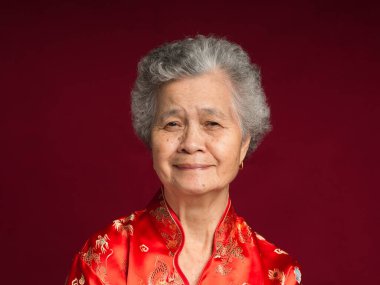 Çin Yeni Yıl konsepti. Geleneksel Cheongsam Qipao elbisesi giymiş, stüdyoda otururken kameraya gülümseyen yaşlı bir Asyalı kadının portresi. Metin için boşluk