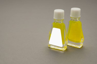 Gri arka planda sarı bitkiler olan küçük şişe kapları. Marka modeli için boş etiket. Doğal güzellik ve sağlık ürünü konsepti. Yan görünüm