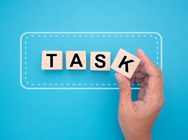 Görev ve program konsepti. Açık mavi arka planda beyaz kenarlı TASK harfleriyle el ele tutuşan tahta küpleri. Üst Manzara. Yakın plan fotoğraf.