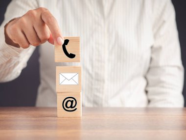 Web sayfası bizimle bağlantı kurar. Elinde ikon sembollü telefon, e-posta, adres olan tahta bir küp var. Mesaj için yer var. İş, pazarlama ve hizmet kavramı