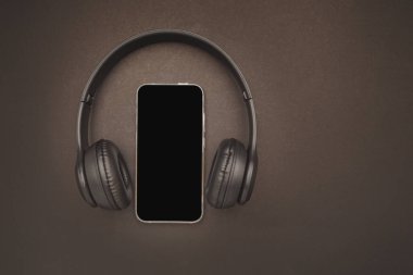 Kablosuz kulaklıklar ve kahverengi arka planda izole edilmiş bir akıllı telefon.