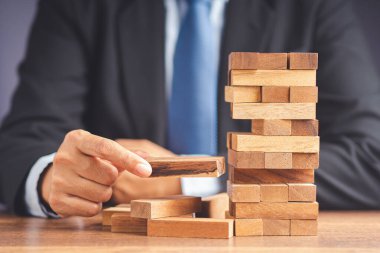 İş büyümesi ve başarı konsepti için yönetim ve strateji planları riski. Çalışma masasında otururken takım elbiseli bir işadamının tahta blok oyunu oynaması. Metin için boşluk