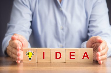 İş yaratıcılığı ve ilham konsepti. Başarı için motivasyon. El, tahta küpleri ampul ikonu ve IDEA harfleriyle korur.