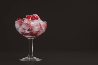 Siyah arka planda vişne suyu ile şarap bardağı. Soğuk içecek ferahlatıcı. Yaz partisi. Masadaki olgun kırmızı acerola kirazı ve yeşil yapraklar. Yüksek C vitamini meyveleri