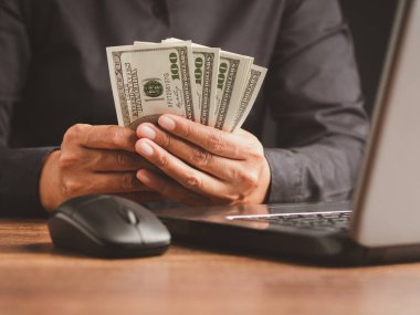 Ofiste masada otururken elinde Amerikan doları banknotu tutan siyah gömlekli bir işadamının eli. Yakın plan fotoğraf. İş ve finans kavramı