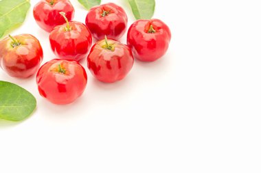 Beyaz bir zemin üzerinde olgun kırmızı acerola kirazı ve yeşil yapraklar yığını. Yüksek C vitamini ve antioksidan meyveler. Üst Manzara. Mesaj için yer var. Yakın plan fotoğraf. Sağlıklı meyve kavramı