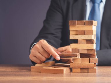 İş büyümesi ve başarı konsepti için yönetim ve strateji planları riski. Çalışma masasında otururken takım elbiseli bir işadamının ahşap blok oyunu oynaması..