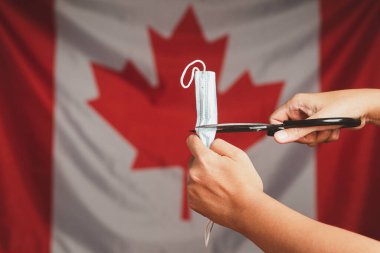 COVID-19 ya da Coronavirus 'un sonu. Kanada bayrağının arka planında bir yumrukta tıbbi maskenin yakın çekimi. Normal hayata dönmek karantinanın sonu