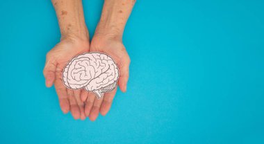 Mavi arka planda, avuç içi yaşlı bir kadının kağıdından yapılmış bir beyin şekli. Alzheimer, Parkinson hastalığı, bunama, felç, nöbet ya da akıl sağlığı. Nöroloji ve Psikoloji