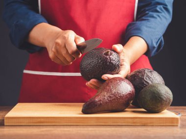 Chef holding a knife cutting avocado on hand while standing in the kitchen. Healthy fruit and food eating concept. Close-up photo clipart