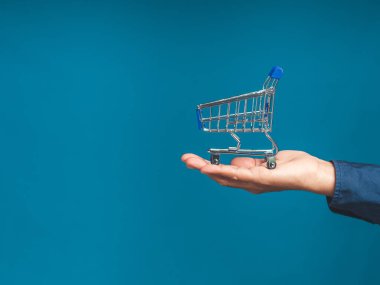 Palmiye insanlarının üzerinde mavi arka planda boş mavi bir alışveriş arabasının yakın çekimi. İş ve e-ticaret kavramı. Yan görüş. Metin için boşluk