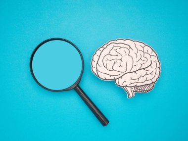 A brain shape made from paper and a magnifying glass on a blue background. Awareness of Alzheimer's, Parkinson's disease, dementia, stroke, seizure, or mental health. Neurology and Psychology care clipart