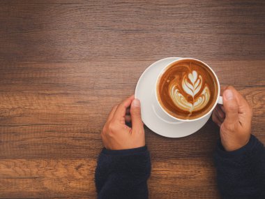 Top view of hand woman holding a fresh coffee cup over wooden table Space for text. Beverage and relaxation concept clipart