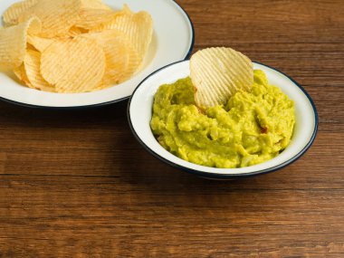 Tahta bir masanın üzerinde beyaz bir tabakta taze guacamole ve patates cipsi ile bir kase. Sağlıklı avokado yayılımı. Üst Manzara. Yakın plan fotoğraf. Geleneksel Meksika hazırlığı kavramı